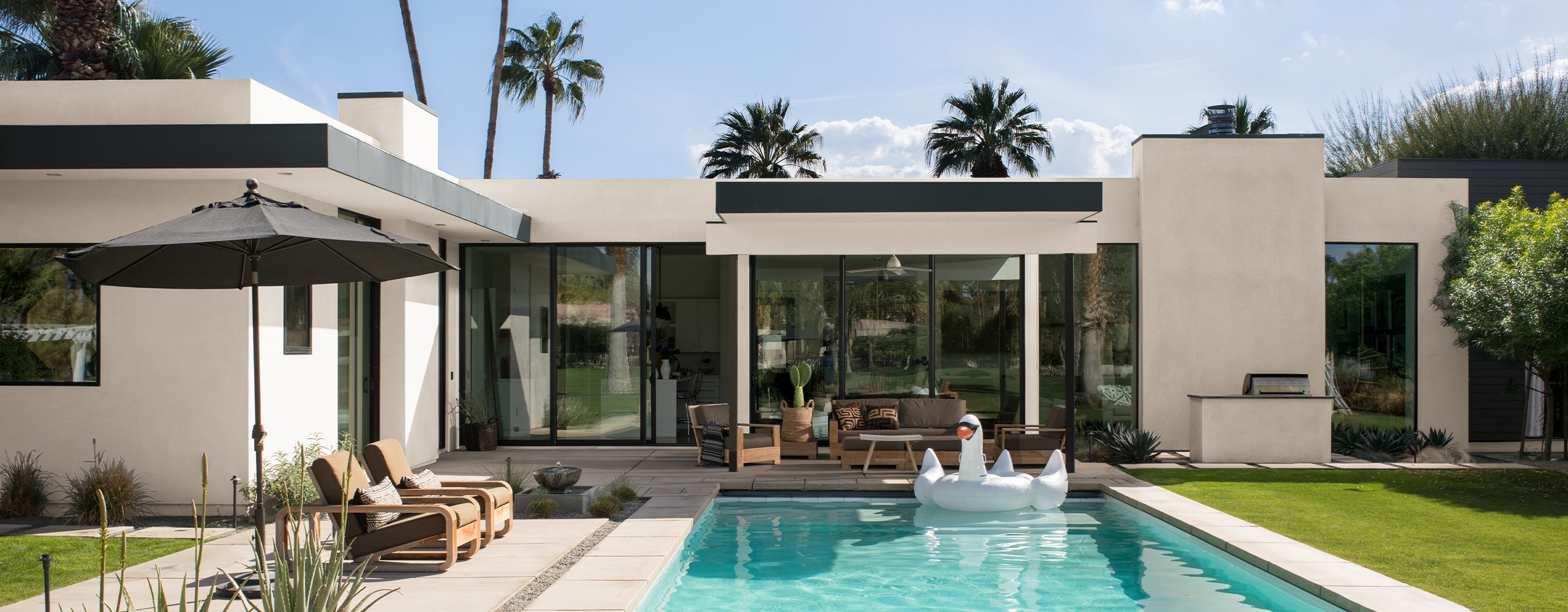 A modern, white-painted stucco house with black trim and palm trees features a beautiful backyard pool and patio.