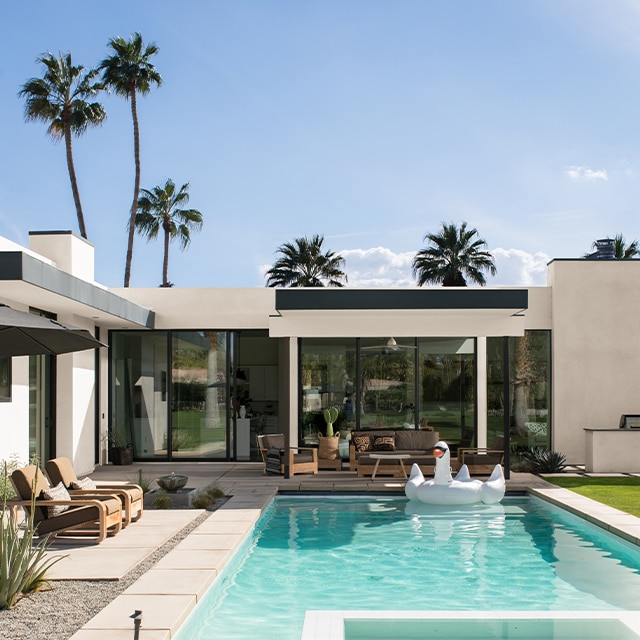 A modern, white-painted stucco house with black trim and palm trees features a beautiful backyard pool and patio.