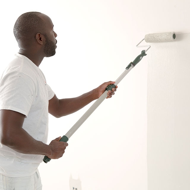 A painting contractor rolling white paint onto a primed wall.