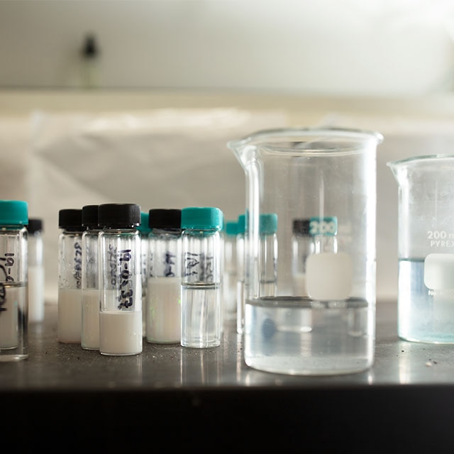 Vials filled with powder and liquid, and two large beakers with liquid, shown in the Benjamin Moore lab.