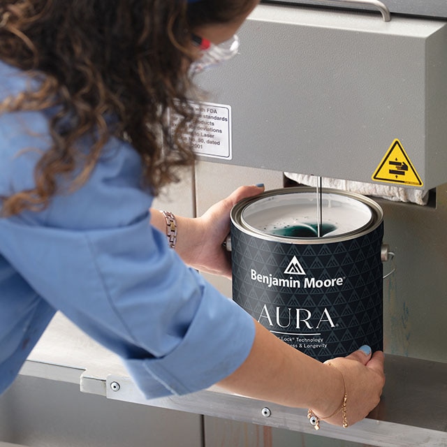 A female lab tech works with an open gallon of Benjamin Moore Aura Interior paint.