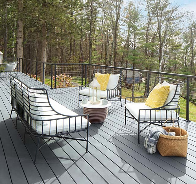 Pretty white cushioned outdoor furniture with yellow pillows on a spacious light gray stained deck.