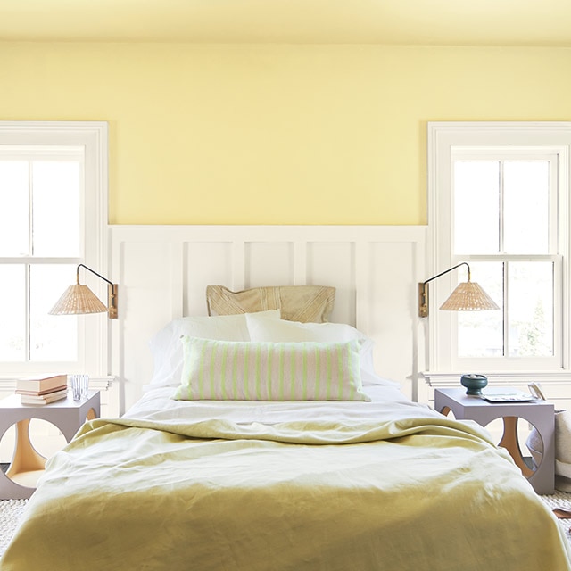 A sunny bedroom with a yellow-painted wall and ceiling, white wainscotting and trim, yellow and white bedding, two reading lamps and side tables.