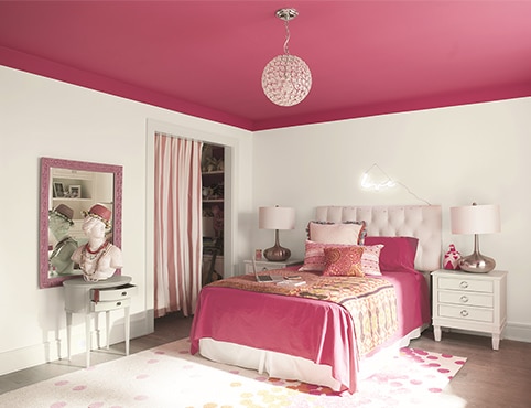 Chambre à coucher avec murs blancs, plafond rose vif et literie rose assortie avec deux tables d’appoint et des lampes.