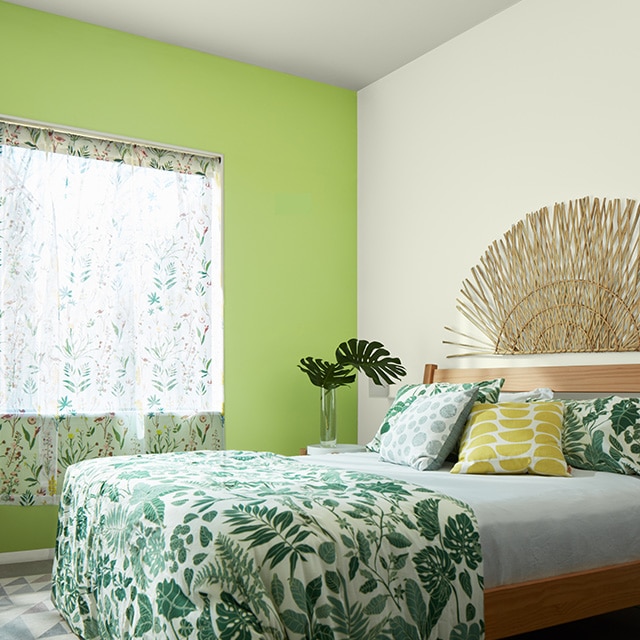 A green-painted accent wall makes a fun statement in this bedroom with white walls, tropical print bedding and curtains, and a wicker art piece over the headboard.