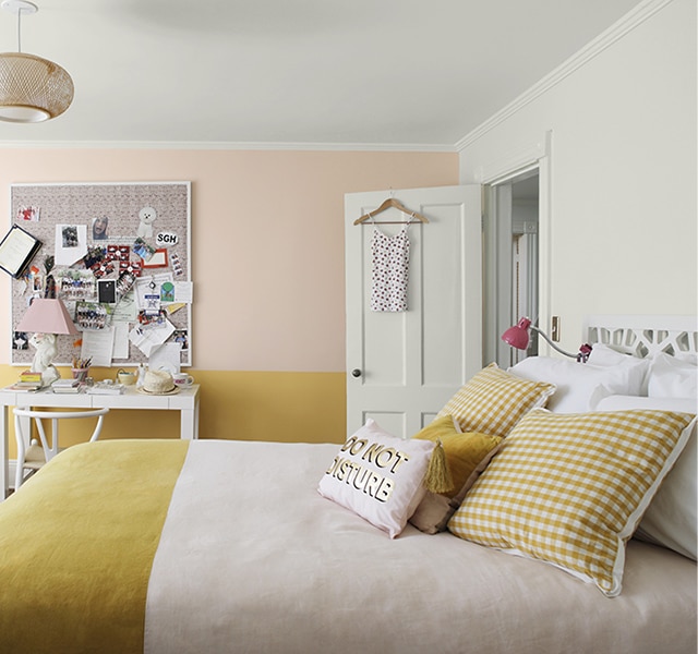 Chambre à coucher rose et jaune avec fauteuil poire, babillard en liège surchargé, bureau blanc et couvre-lit avec articles de literie en deux tons.