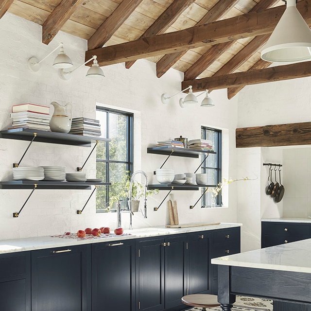 A large, open kitchen with white-painted walls, a wood vaulted ceiling, and gorgeous lower cabinetry painted in a striking denim blue color.