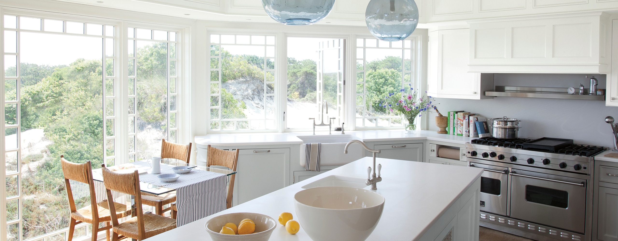 Bright, airy kitchen with centre island and cliffside view, off-white-painted walls, and a light blue-painted ceiling.