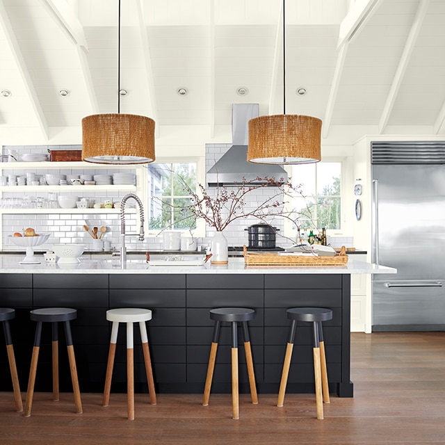 A bright, open kitchen with an off-white painted vaulted ceiling, white subway tile backsplash, open shelving, a large island with a black-painted base and white countertop, and fun black-and-white wooden bar stools.
