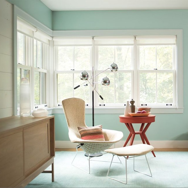Le coin d’un joli salon bleu-vert pâle avec des moulures gris pâle, plusieurs fenêtres et des meubles contemporains.