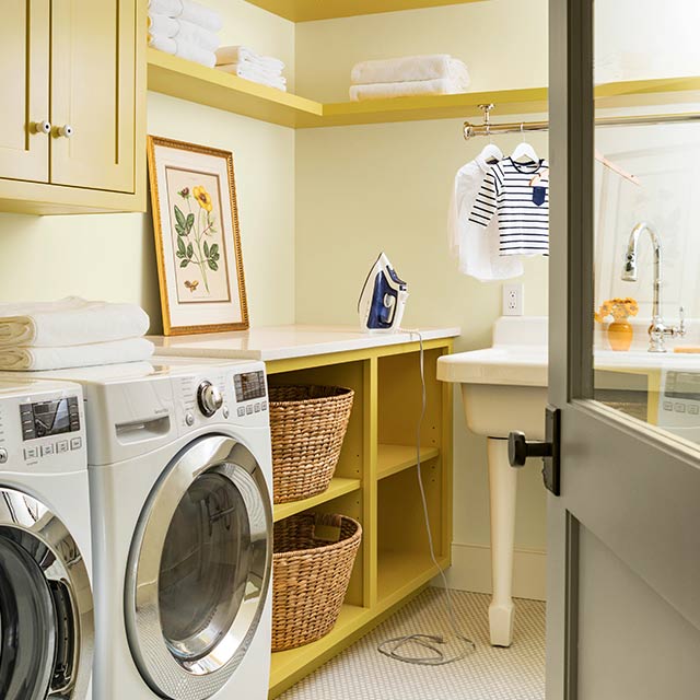 A cream laundry room with built-in shelves and cabinets in a midtone yellow color.  