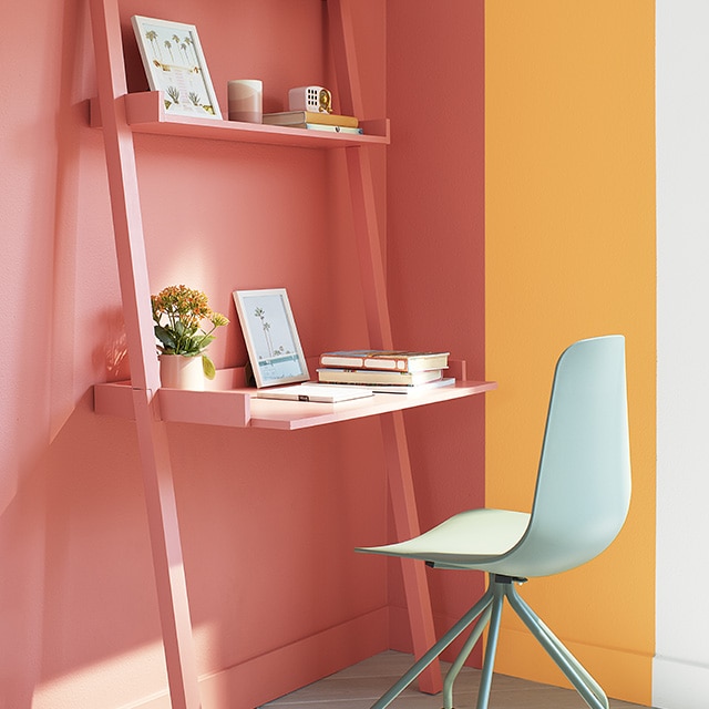 A cheerful corner office space with a large orange rectangle overlapping a golden yellow rectangle painted on white walls, with an orange desk and shelves, and a light green swivel chair.