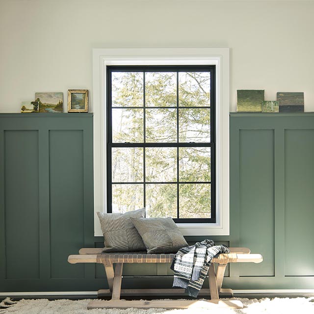 Vestibule au lambris d’appui vert foncé avec moulures et murs blancs, grande fenêtre et banc avec jeté et coussins.