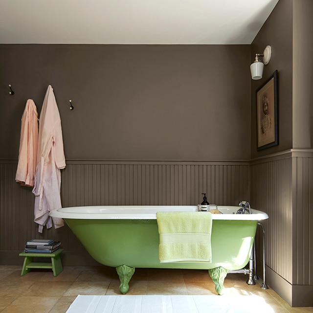 Les murs d’une salle de bains peints en brun contrastent avec une baignoire sur pieds verte.