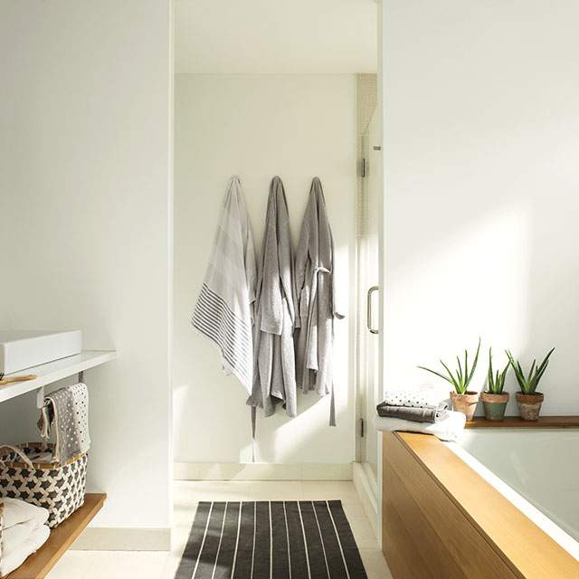 Une salle de bains peinte en blanc arborant des peignoirs gris, une baignoire à cadre en bois, des paniers de style boho et deux lavabos.