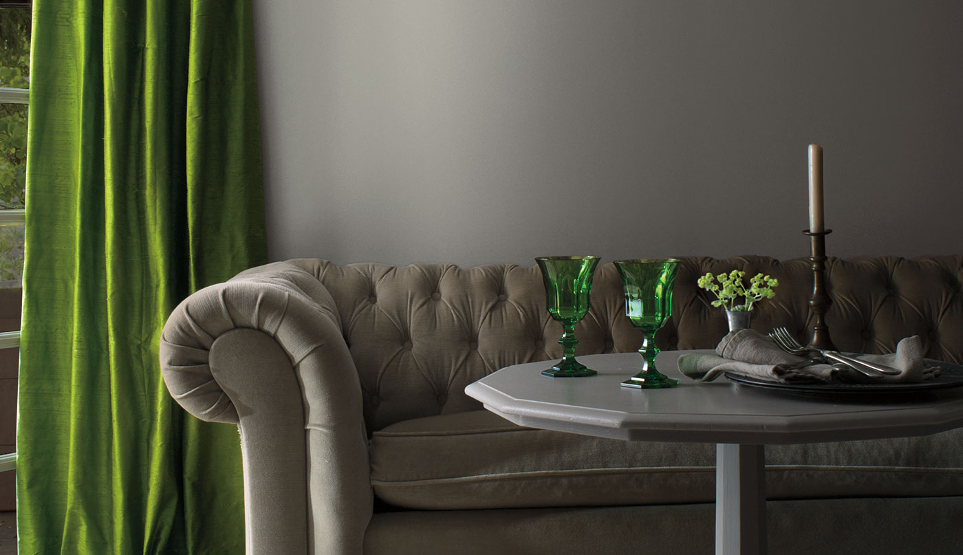 Un salon aux murs peints en gris décoré d’un canapé gris de style traditionnel, d’une table grise présentant des accents verts et de rideaux en velours verts.