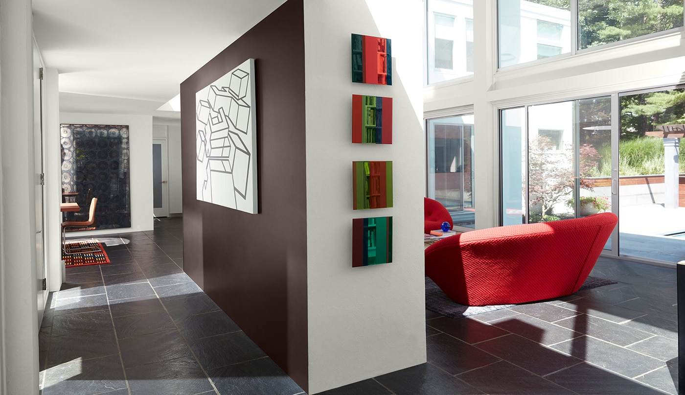 Une pièce de style rétro arborant des murs et un plafond peints en blanc, un mur d’accent brun, de grandes fenêtres et un fauteuil rouge.