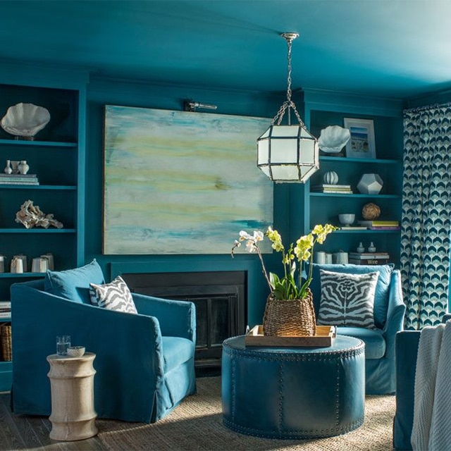 An all-blue painted living room with blue club chairs and built in shelving.