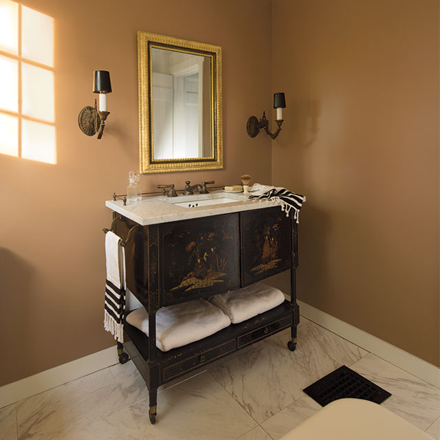 A light orange-painted bathroom with classic sink, gold mirrors, and two wall lights.