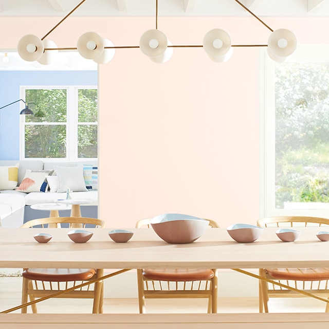 Une salle à manger aux murs peints en rose clair décorée d’une longue table en bois, de chaises assorties et de bancs.