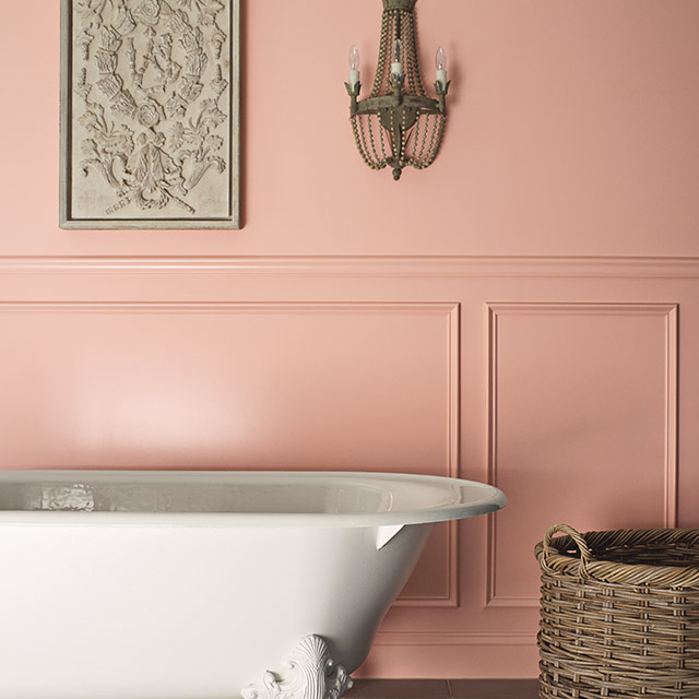 Un mur de salle de bains peint d’un rose soutenu avec des lambris assortis et une baignoire sur pieds blanche.