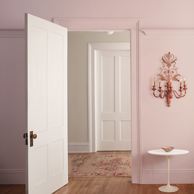 Des murs peints en rose clair avec une porte ouverte donnant sur une pièce aux murs peints en blanc cassé.