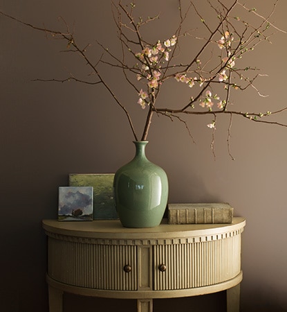 A painted hallway in taupe Weimaraner AF-155 with demi-lune table and jade vase holding flowering branches.