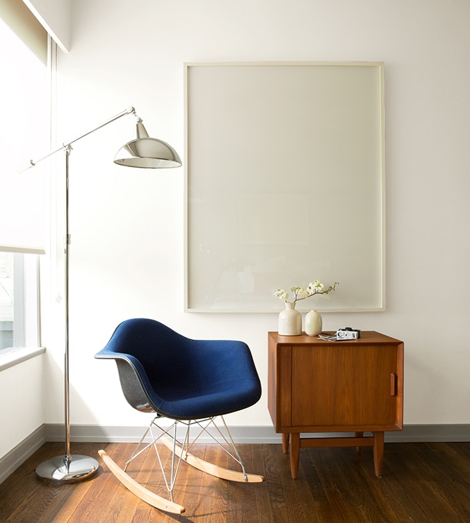 Un fauteuil berçant bleu, une table d’appui moderne des années 1950 et une lampe chromée sur pied de style contemporain agrémentent le coin de cette pièce.