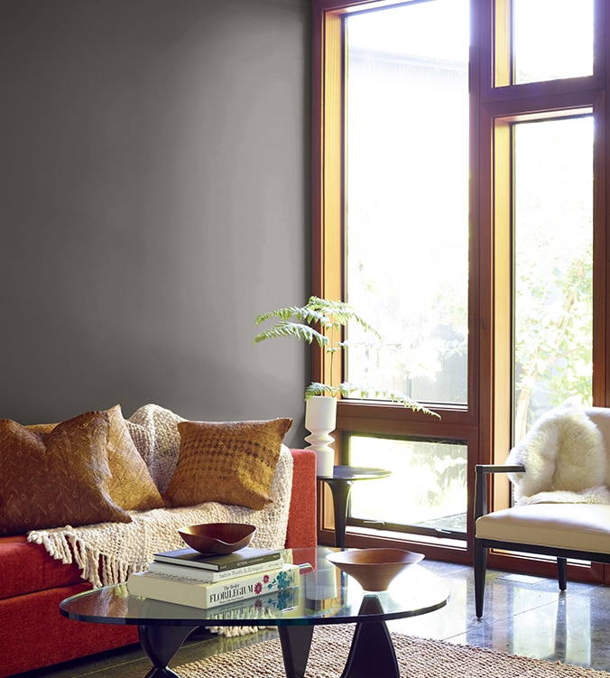 Boudoir contemporain avec fenêtres pleine longueur, table basse en verre de style moderne et canapé orangé avec jeté de couleur crème.