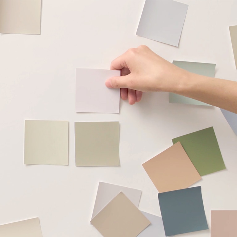 A person applying various color swatches on a white wall.
