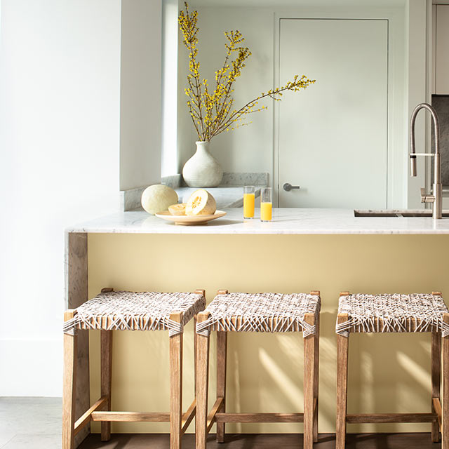 Small kitchen with white-painted walls, a yellow kitchen island and three rattan barstools.