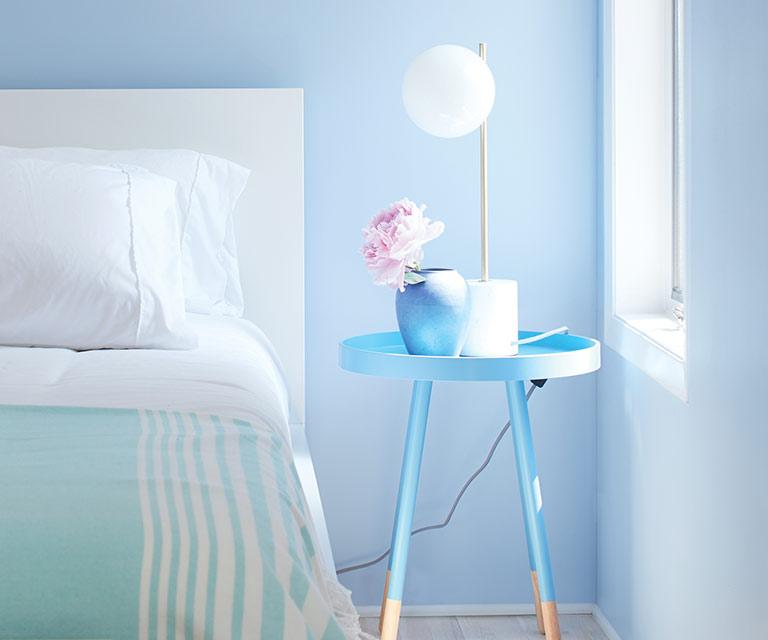 A blue-painted bedroom with blue and white bedding, light wood floors, and a blue night table.