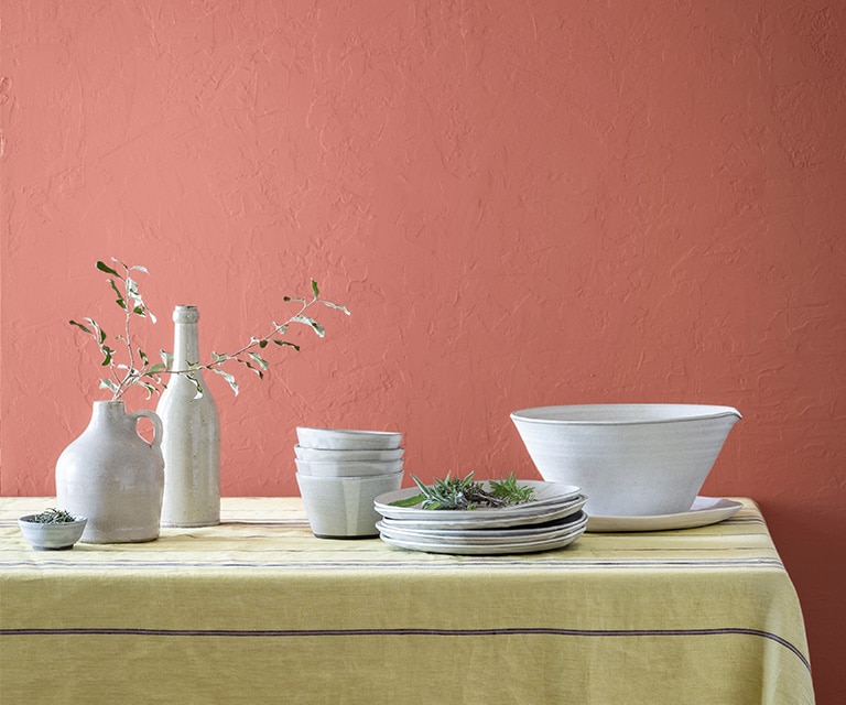 Des vases décoratifs et des bols de service blancs sur une table devant un mur peint d’un rouge doux.