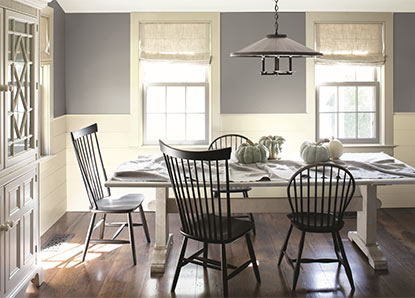 A pale gray-painted dining room, detailed with white wainscotting and black colonial-style chairs.