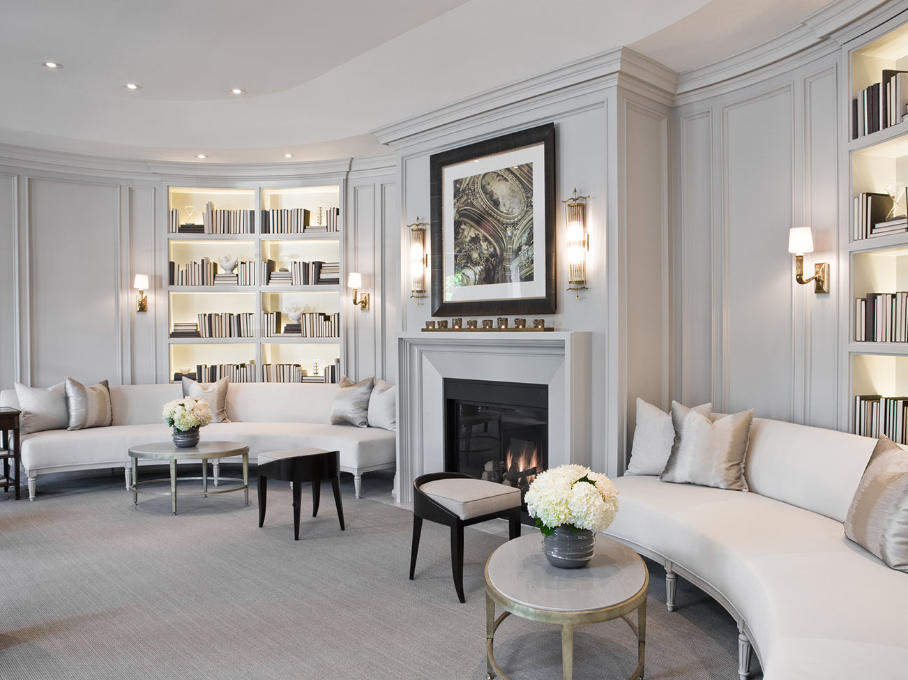 An elegant living room with wall sconces, two matching light gray sofas, and built-in bookcases on each side of a gray fireplace.