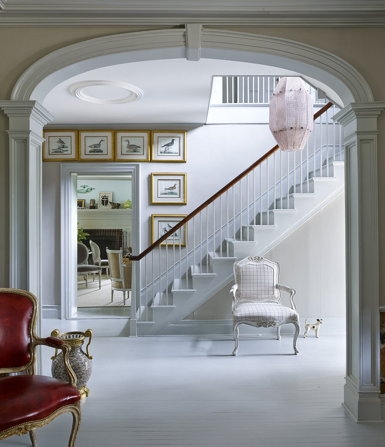 Elegant staircase viewed through ornamental arch with framed walls prints at base of stairs.