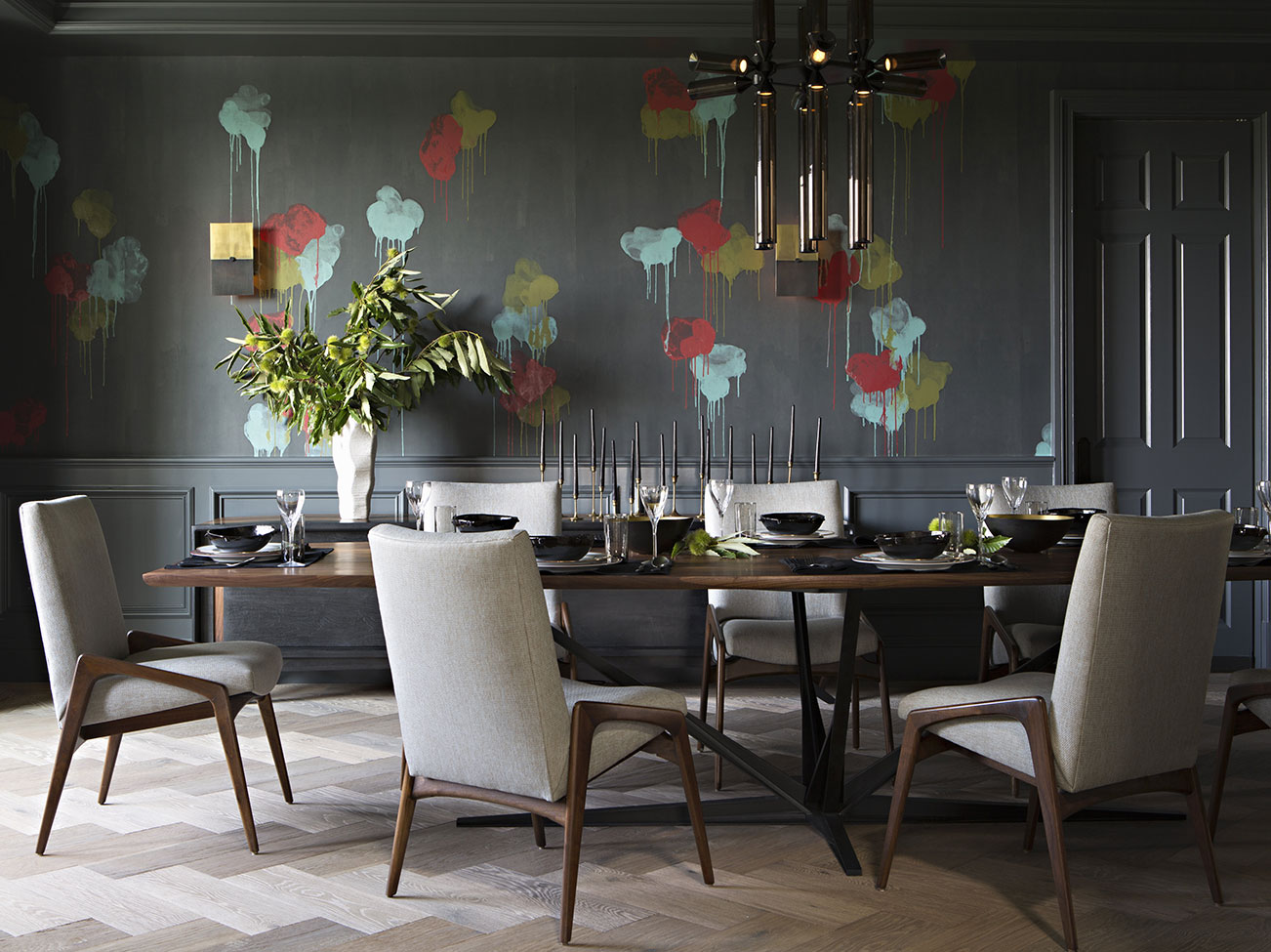Salle à manger moderne aux murs gris avec éclats multicolores, tapis taupe à chevrons et chaises beiges à cadre en bois de style danois.