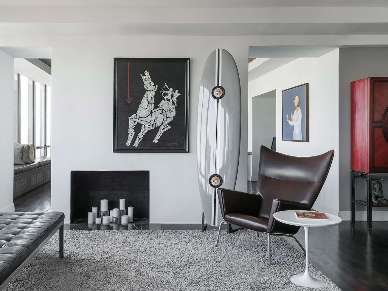 Boudoir lumineux aux murs blanc cassé avec banc touffeté en cuir gris, cheminée et fauteuil moderne en cuir.
