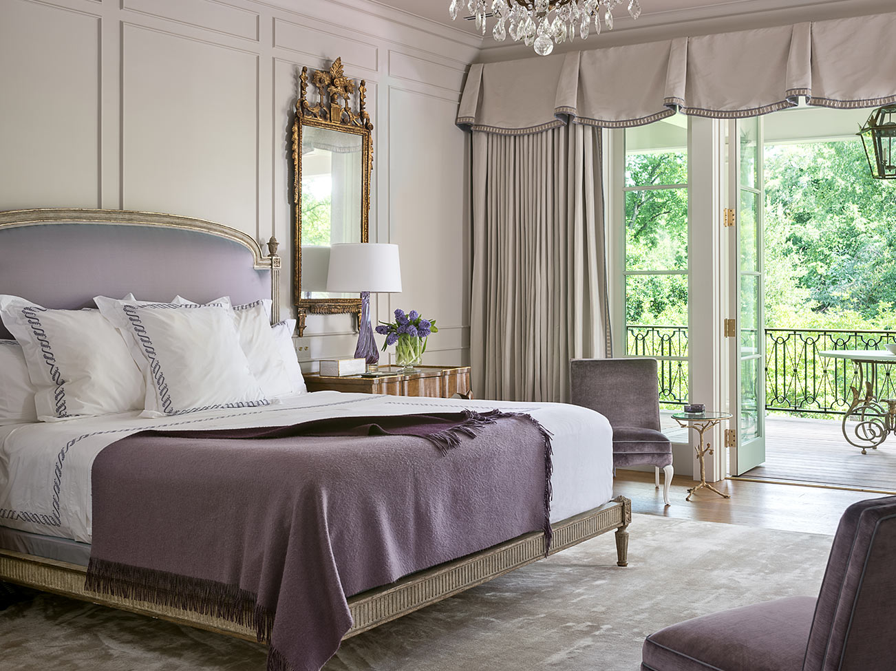 Glamorous light gray and pale lavender bedroom, panelled walls, large king bed, draped windows and door open to terrace.