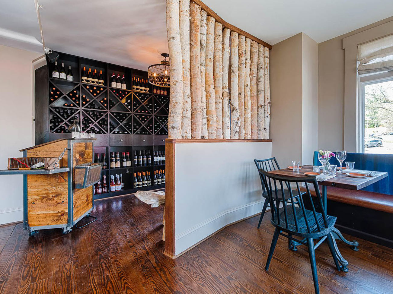 A wine room and office area, separated by a small curved wall, wood floor, and blue-painted chairs.