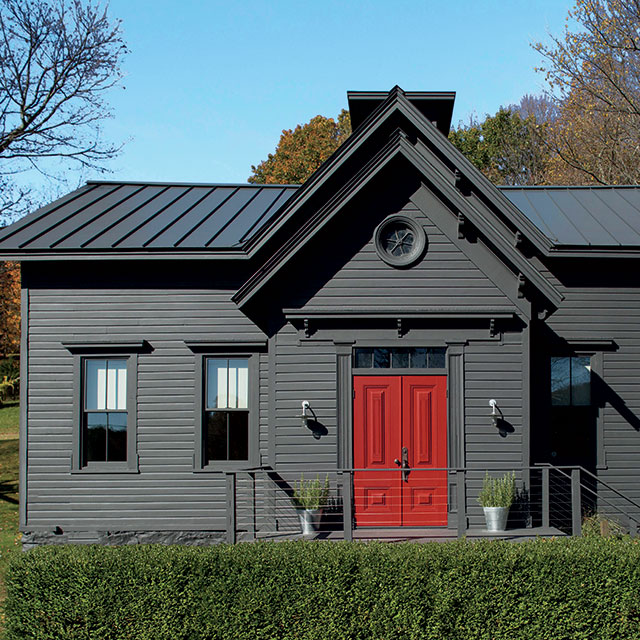 A home with a dark red-painted front door adds a pop of color to a gray-black-painted exterior.