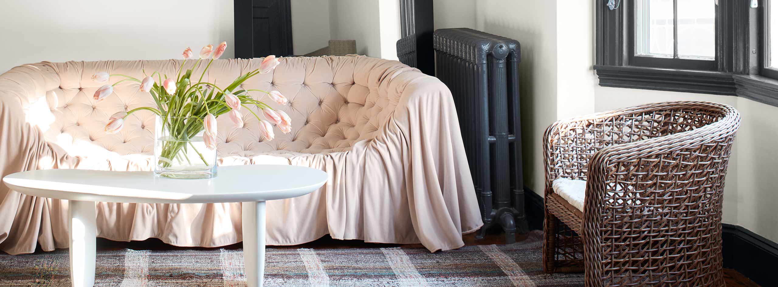 Salon blanc avec moulures noires et radiateur noir avec sofa rose, petit tapis en tissu écossais et lustre chandelier moderne.
