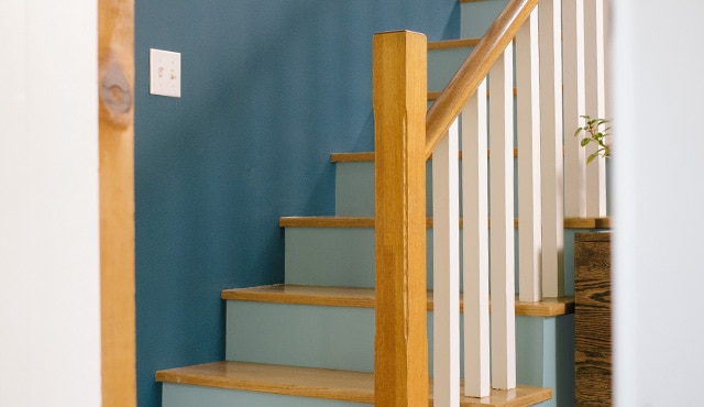 Escalier avec mur bleu, contremarches bleu pâle, balustres blancs et plans de marche et rampes en bois naturel.