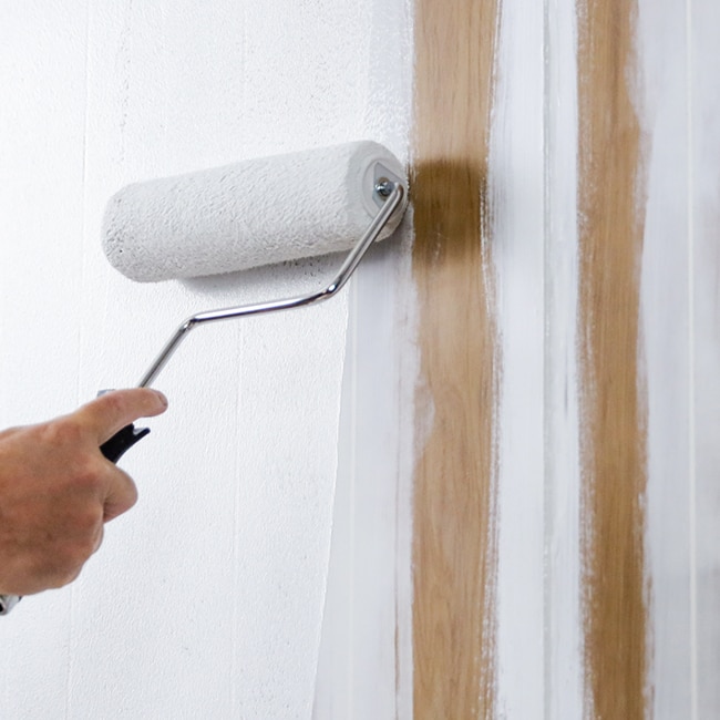 A homeowner rolls paint onto a wood paneled wall.