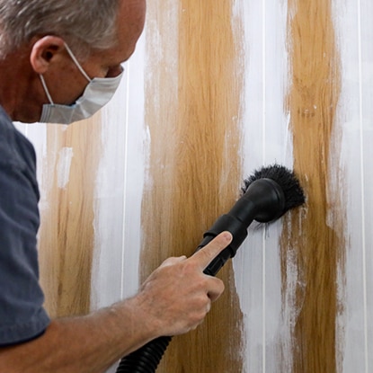 A homeowner wearing a dust mask sands the caulked grooves of wood paneling.