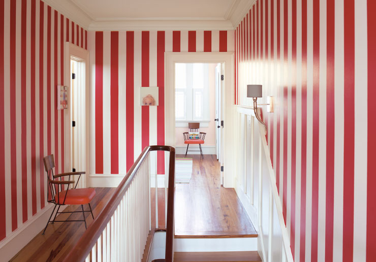 Couloir avec murs à rayures rouges et blanches, chaise des années 1950, œuvre murale originale, moulures et lambris blancs et escalier.