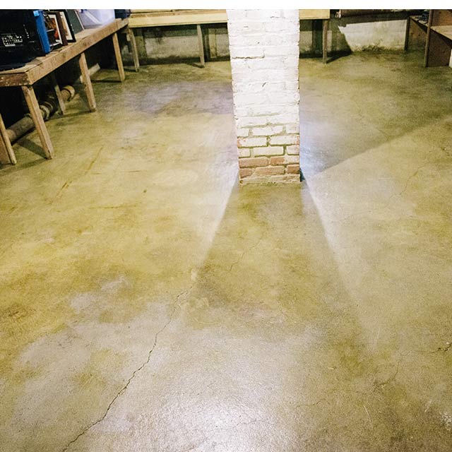 A concrete floor that has been sealed. A brick column is in the middle of the room.