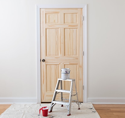 Un escabeau, un pot de peinture et des outils devant une porte et un mur correctement préparés.