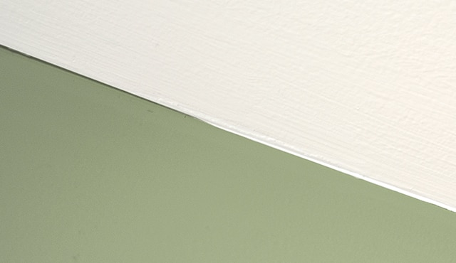 Un gros plan sur la jonction entre un plafond blanc et un mur vert.