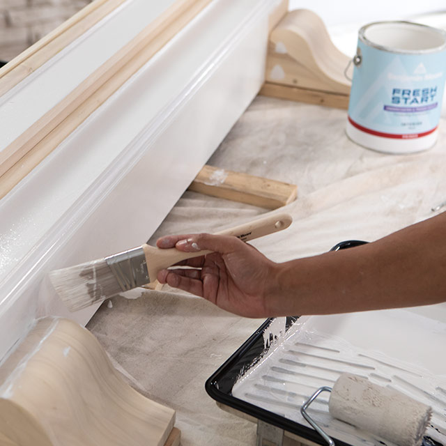 A homeowner using a paintbrush to apply Fresh Start® primer to a floorboard.